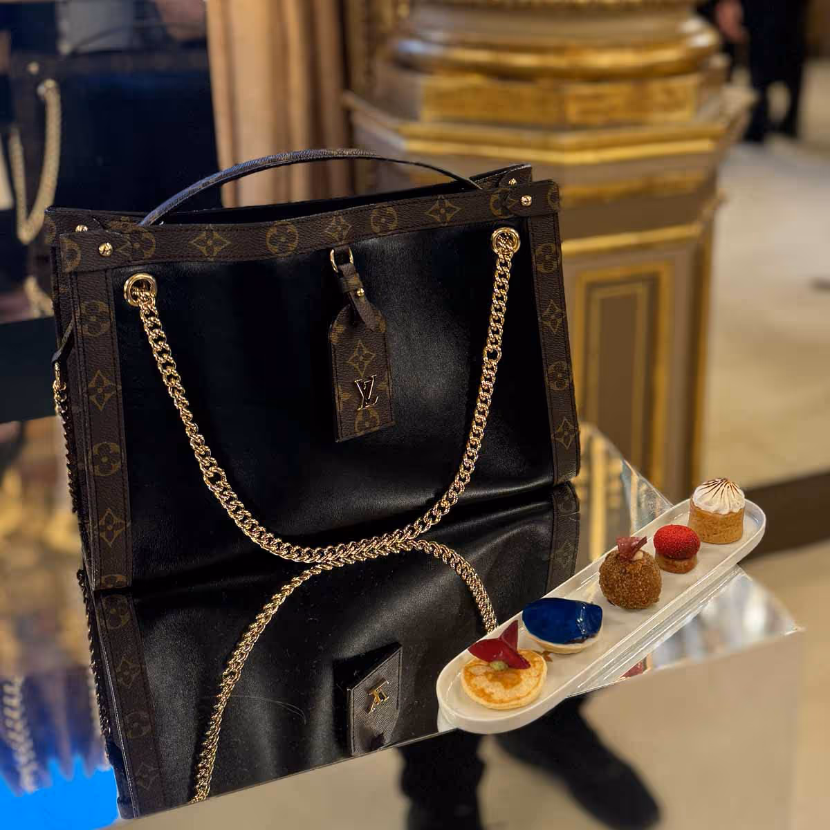 Black Louis Vuitton bag with a gold chain next to elegant desserts